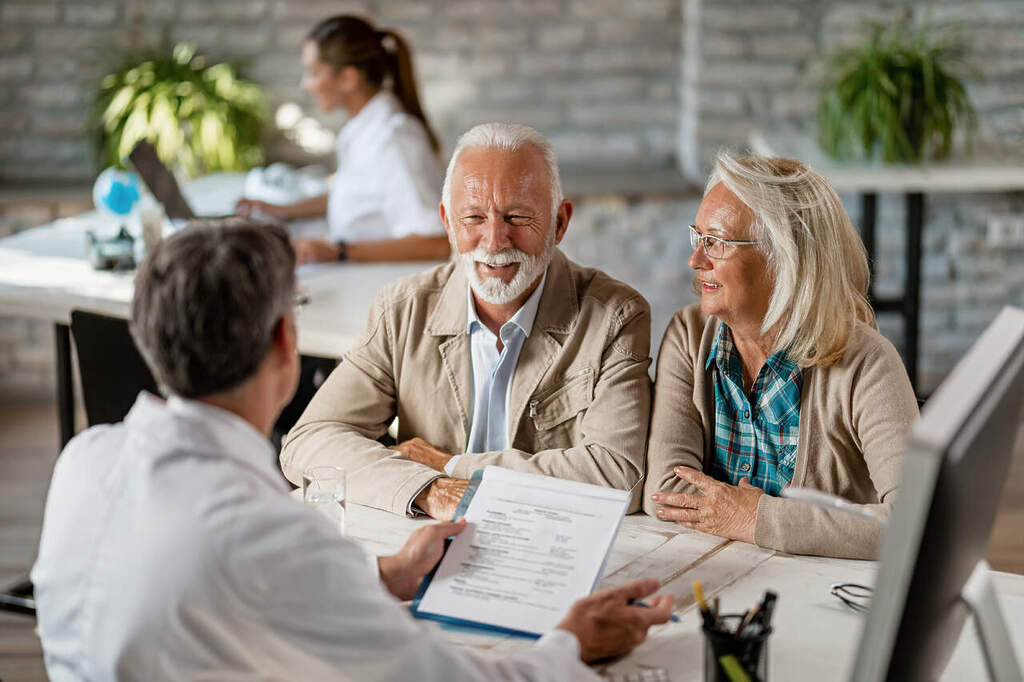 Happy senior couple communicating with a doctor about their health insurance while going through paperwork.