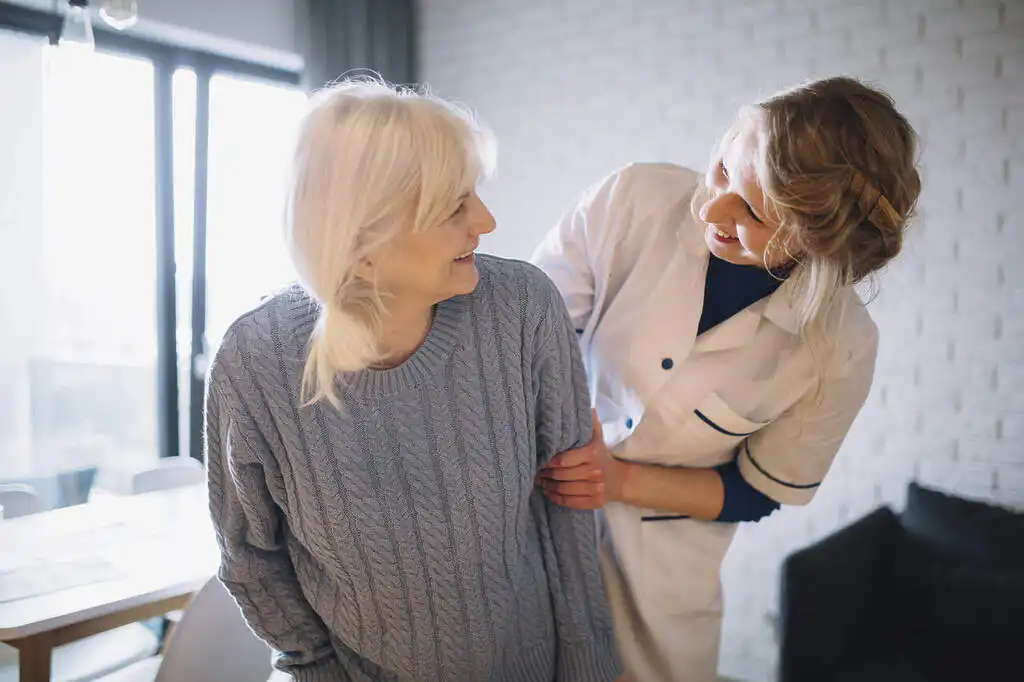 Elderly person being cared for in a home environment, with a health professional smiling
